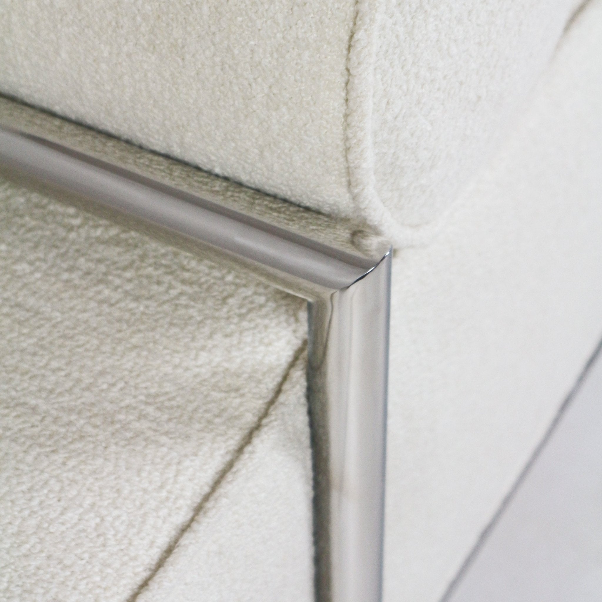 Close-up of a white boucle upholstered bench showing textured fabric and a polished stainless-steel frame corner and joint.
