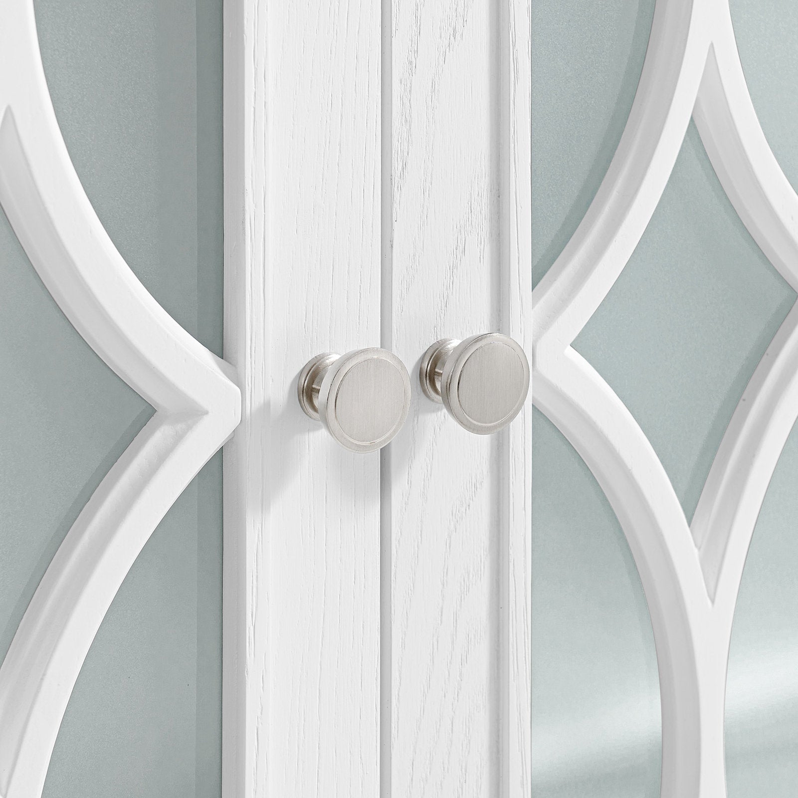 Close-up of white painted solid wood vanity doors with decorative curved overlay, frosted stone-gray glass panels and two round brushed-nickel cabinet knobs.