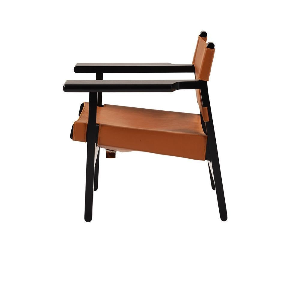 Side view of a modern lounge chair with a black solid wood frame and tan leather sling seat and back, featuring straight armrests and minimalist angled legs.