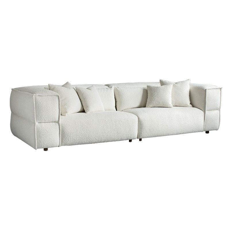 Low-profile white boucle sectional sofa with deep cushioned seats, rounded block arms, four matching throw pillows and short dark wooden legs on a white background.