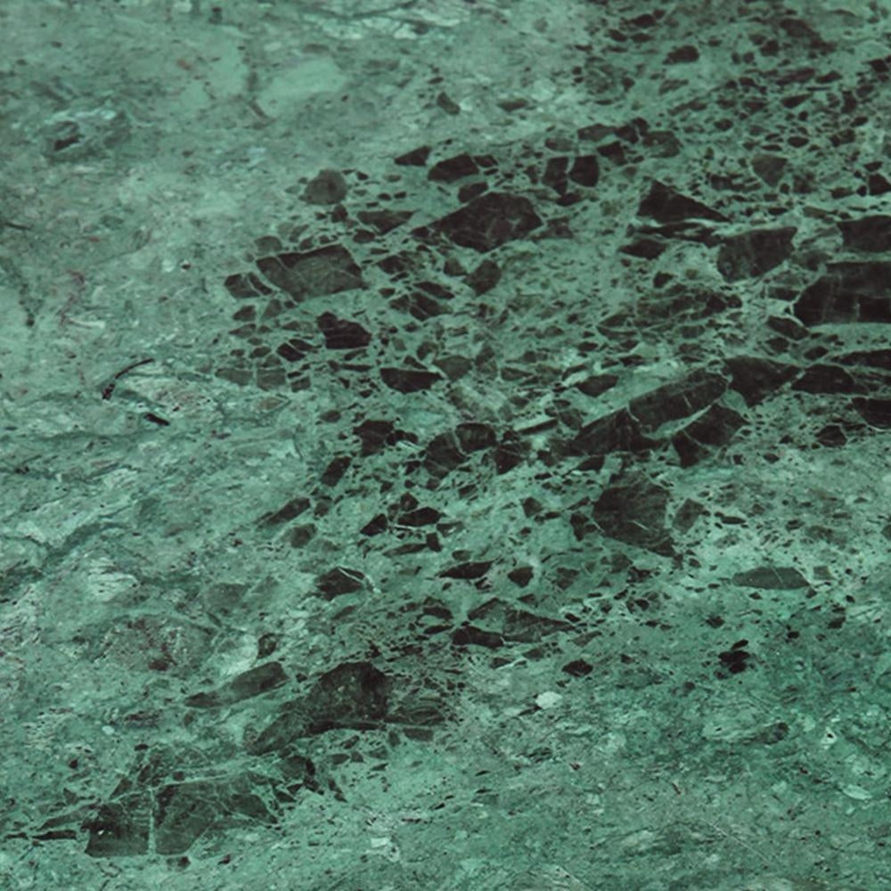 Close-up of a green marble tabletop with deep black veining and scattered stone fragments on a polished surface, highlighting the modern coffee table's natural stone texture.