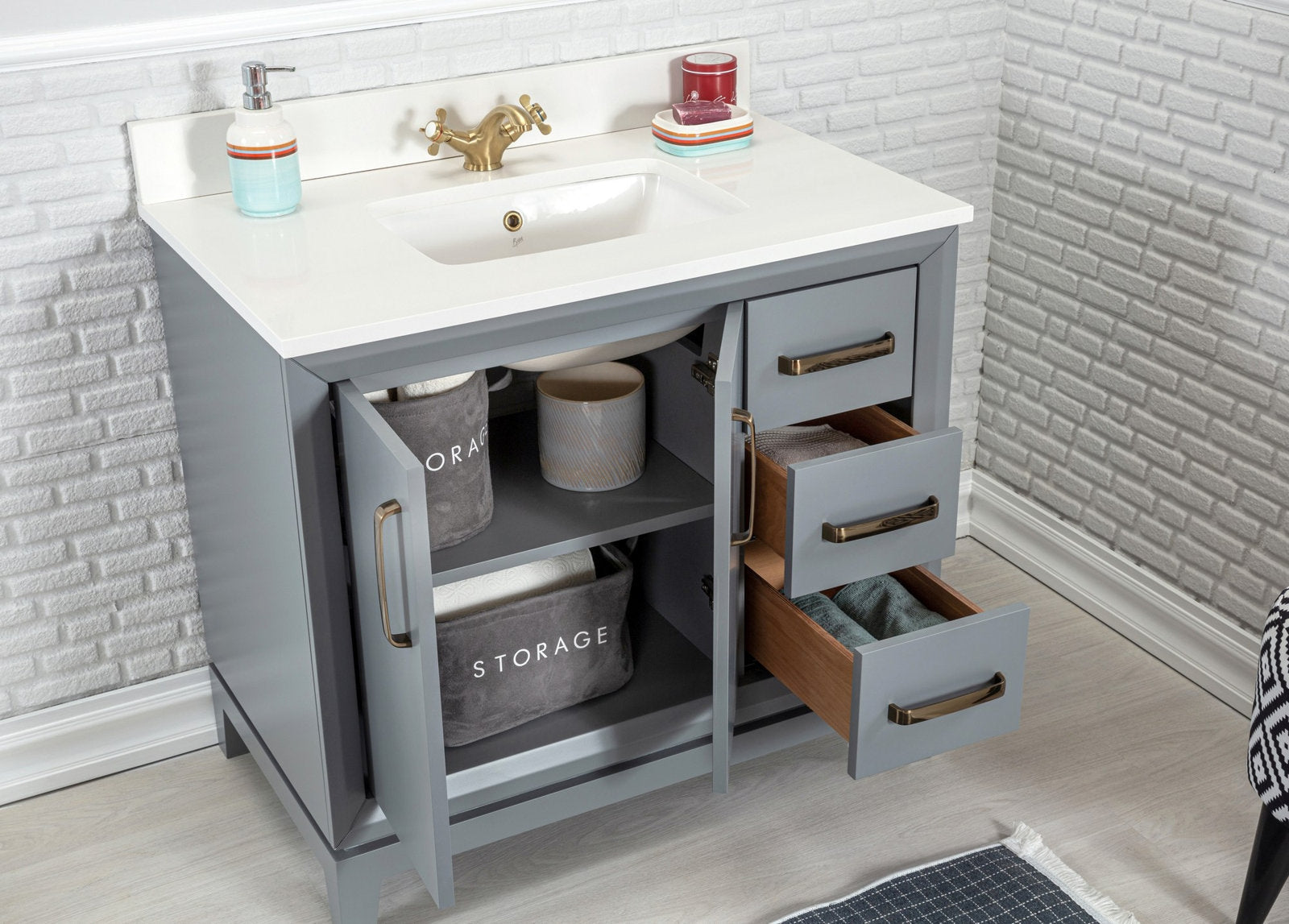 Modern gray solid-wood bathroom vanity with a white stone countertop and integrated ceramic sink, antique brass faucet and hardware; two open cabinet doors and three partially open drawers revealing wood interiors and fabric storage bins.