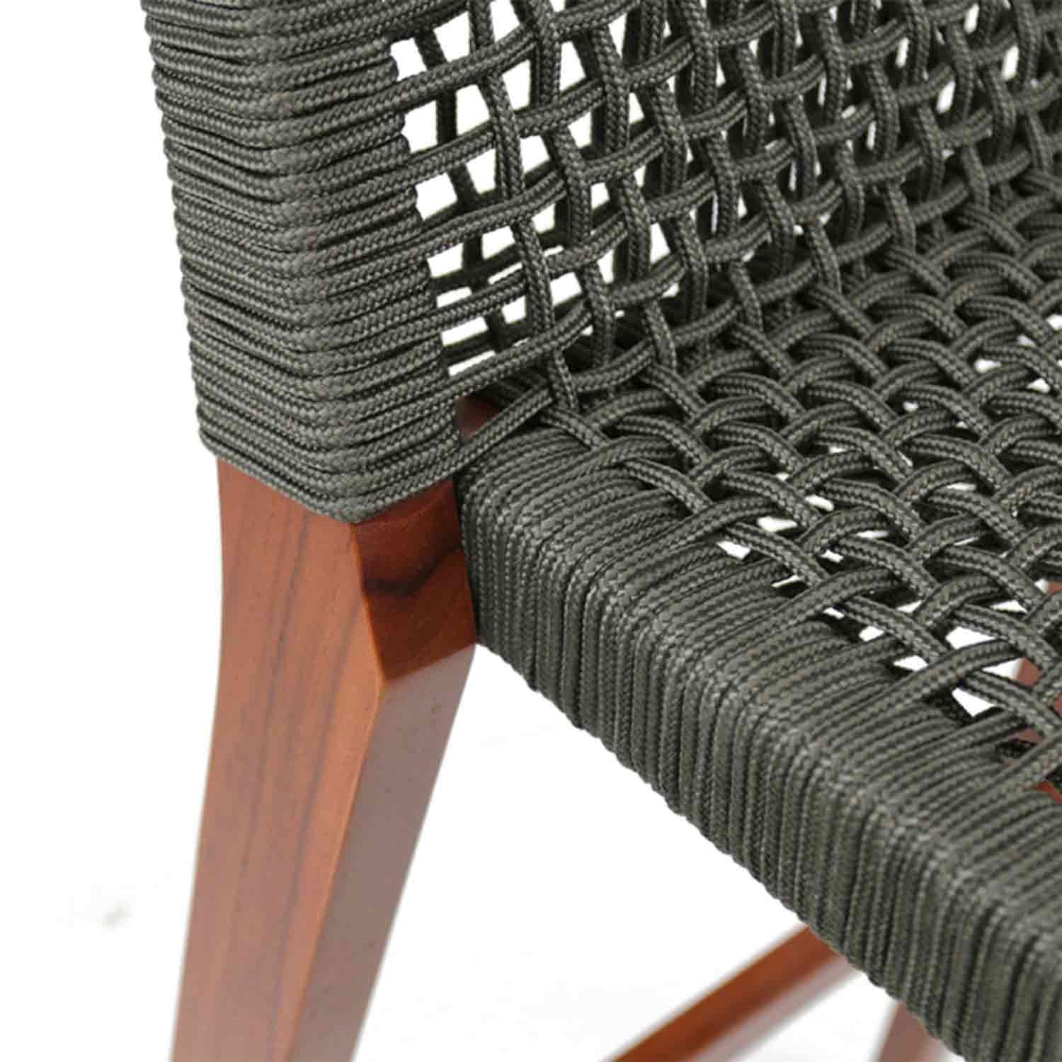 Close-up of dark gray woven rope seat and back wrapped around a solid teak bar stool leg, showing braided texture and tight woven pattern on an outdoor coastal-style armless stool.