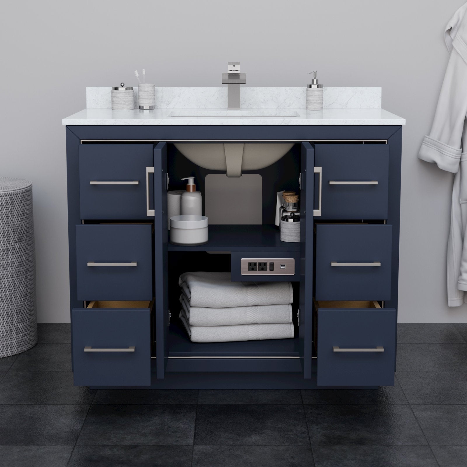 Modern 42-inch solid wood bathroom vanity with white stone countertop and integrated rectangular sink, navy cabinet with brushed-nickel bar pulls, six drawers and open center storage showing towels, toiletries and a built-in outlet.