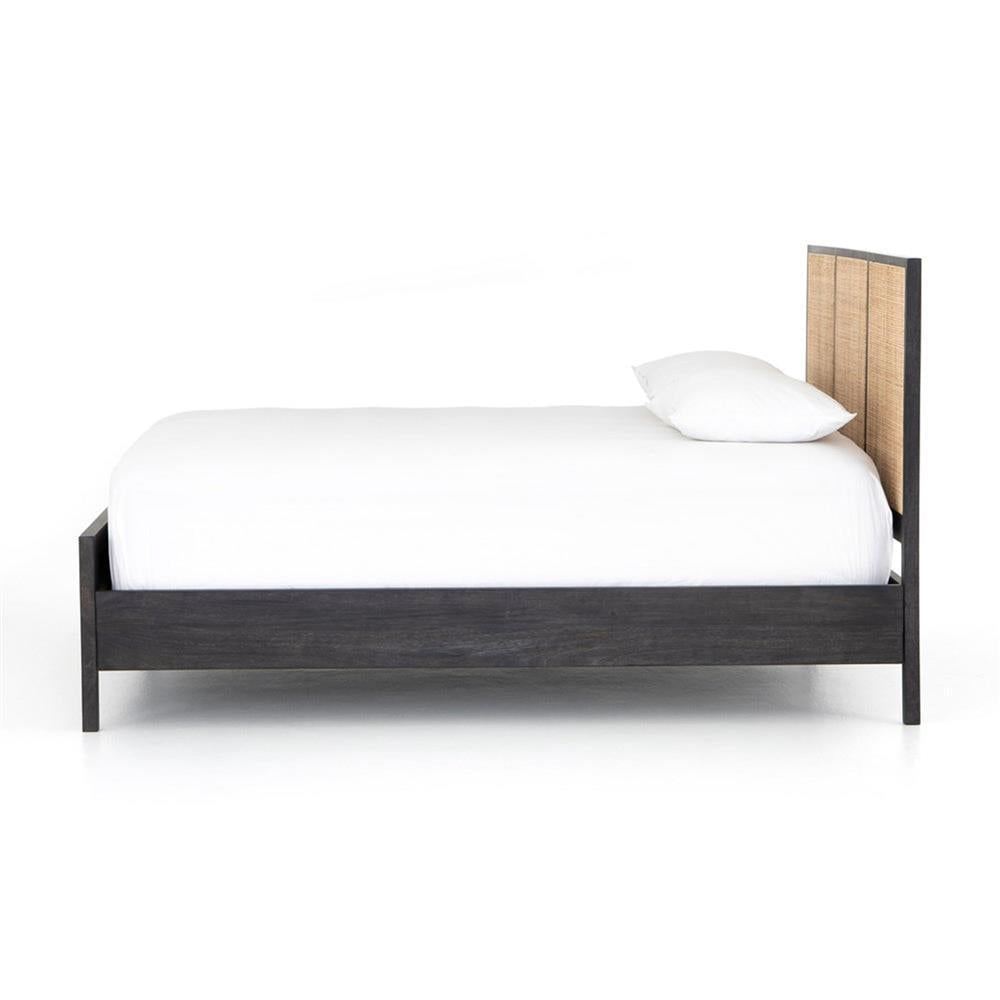 Side view of a teak wood platform bed with a dark-stained frame and woven rattan headboard panel, dressed in white bedding and a single pillow on a white background.