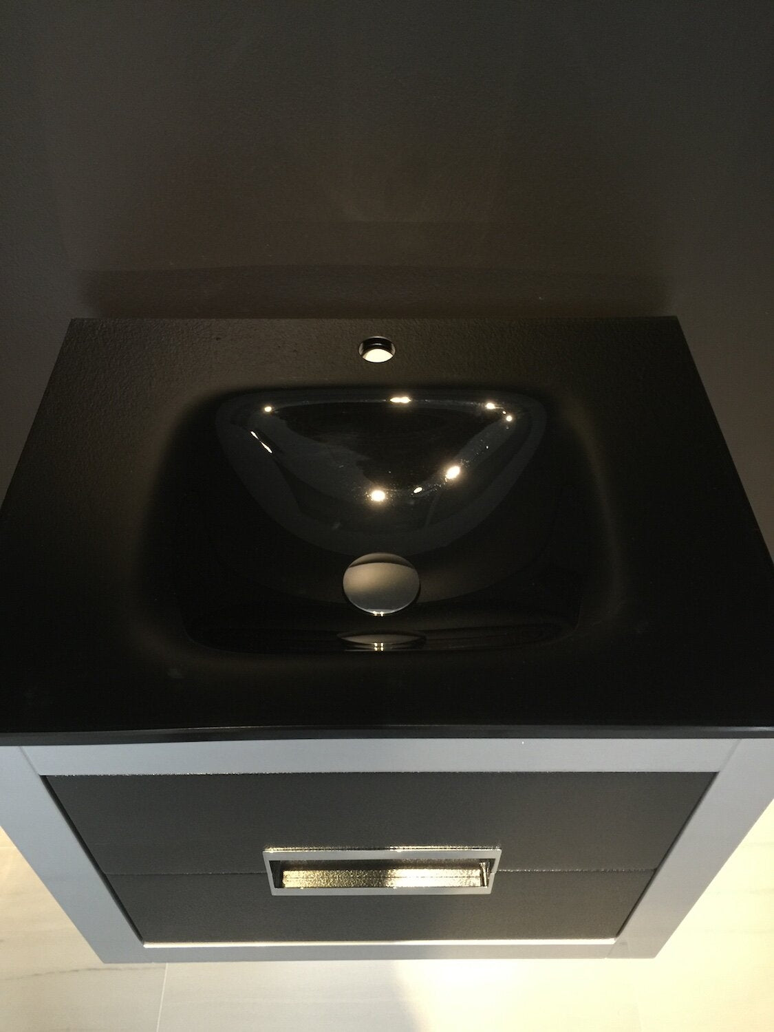 Top-down view of a modern solid wood bathroom vanity with a stone-colored top and glossy black ceramic sink, single faucet hole and chrome rectangular drawer pull.
