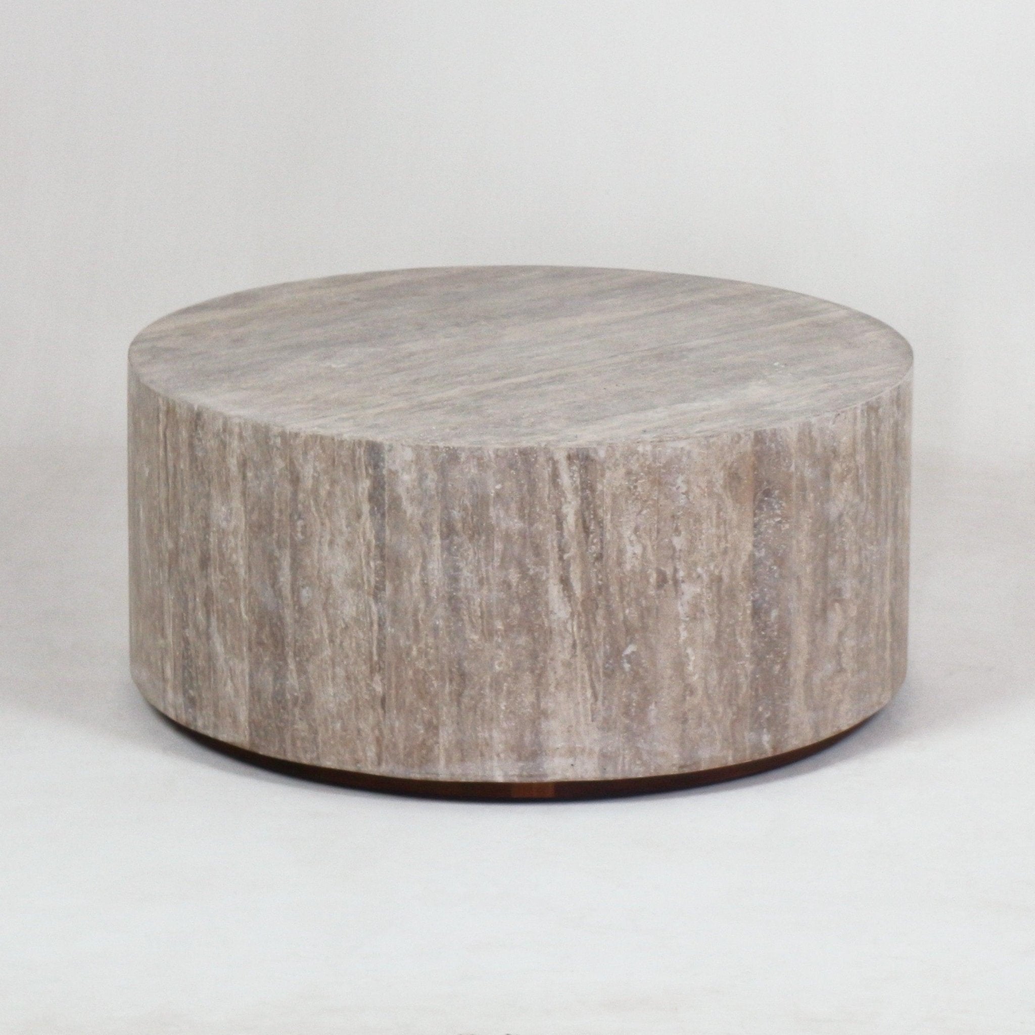 Low round travertine coffee table in natural beige with vertical veining and a slim metal plinth base, shown on a neutral studio background.