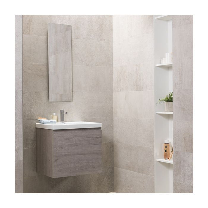 Modern floating solid-wood vanity in a stone-colored finish with a white ceramic sink and chrome faucet, mounted on stone-look tiled wall beneath a tall mirror and next to recessed shelving with toiletries.
