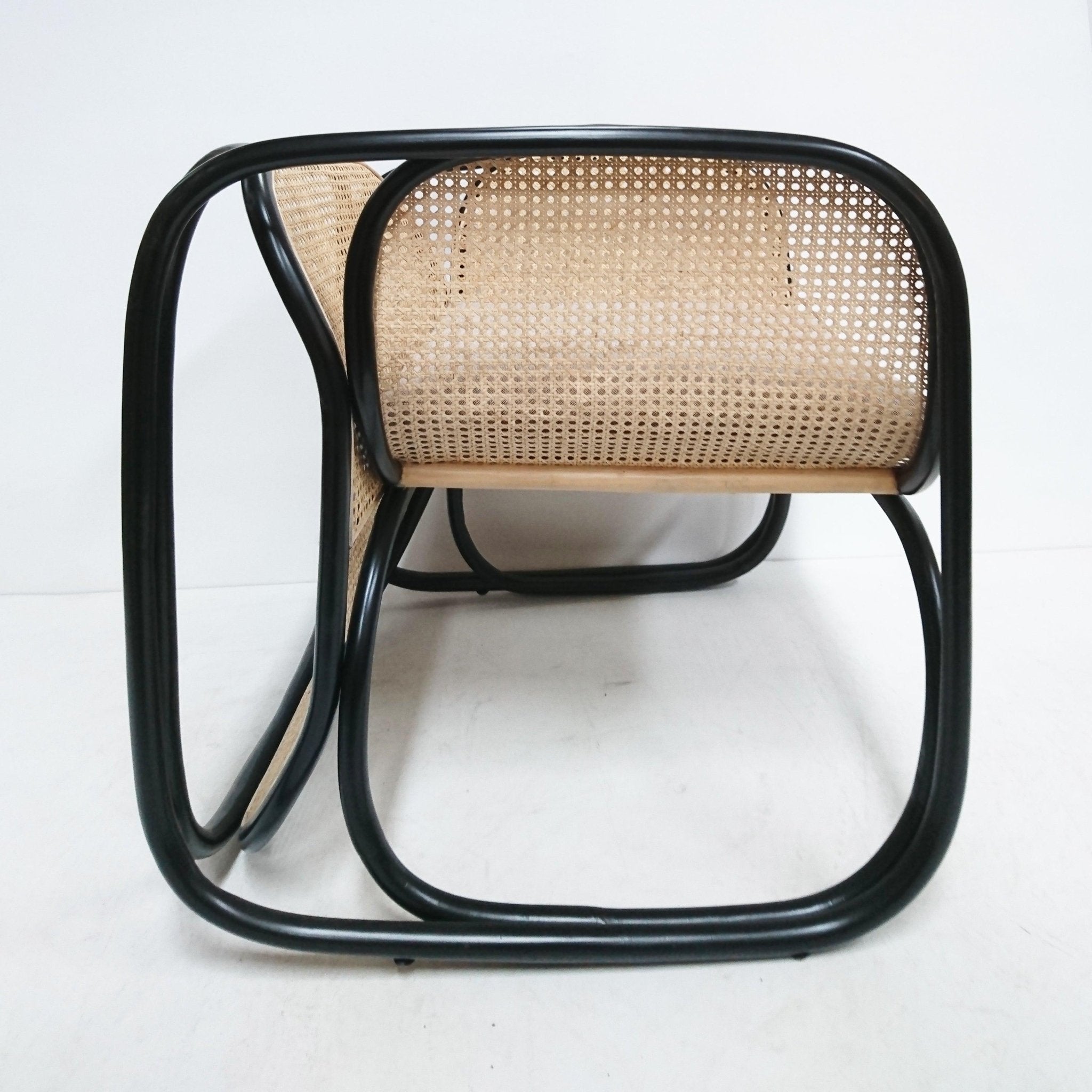 Low-angle view of a modern contemporary lounge chair with a curved black metal tubular frame and natural cane rattan seat and back, highlighting the looped base and woven cane pattern.