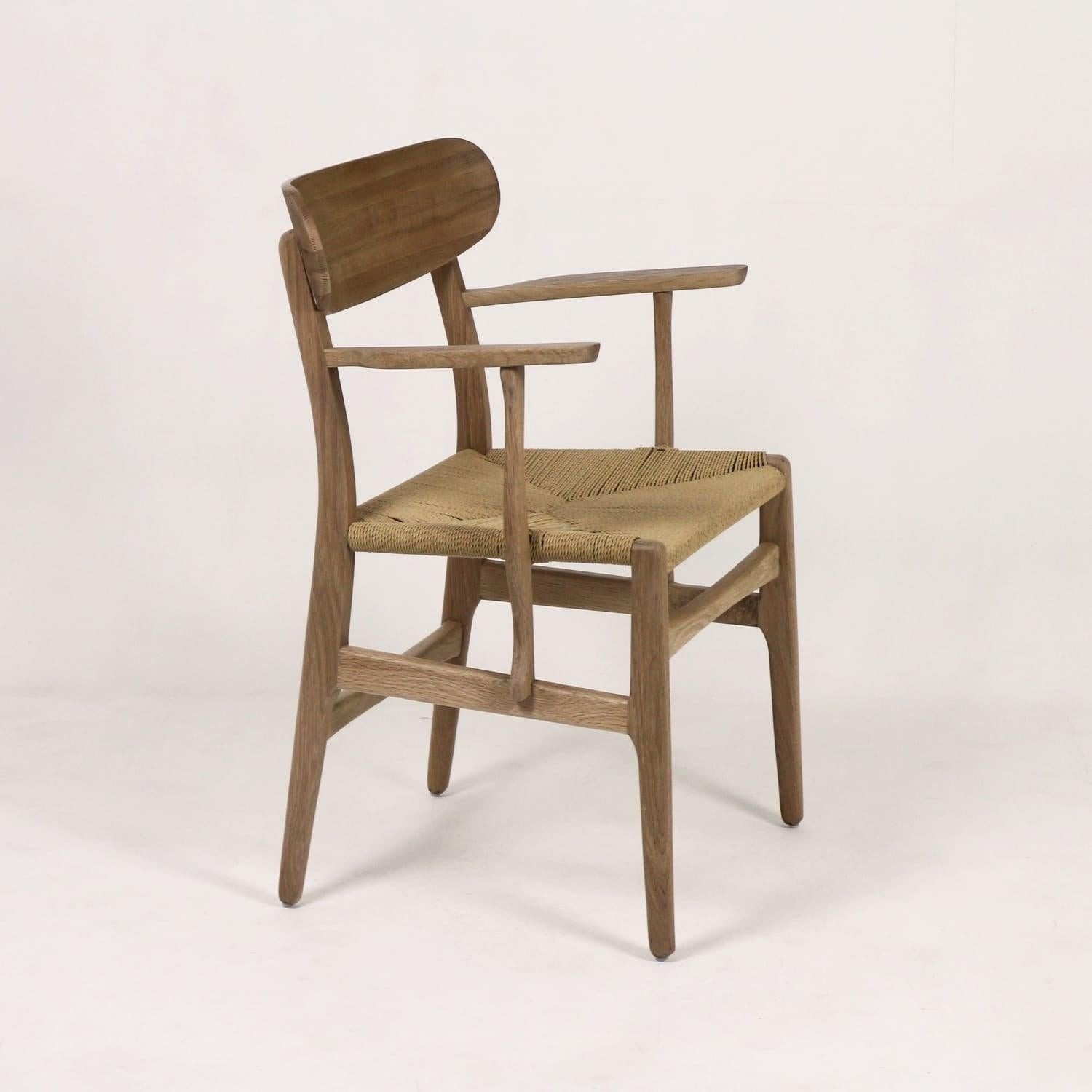 A solid wood dining chair with a curved wooden backrest, woven rope seat and slender armrests in a natural oak finish, Scandinavian-modern styling shown on a neutral studio background.