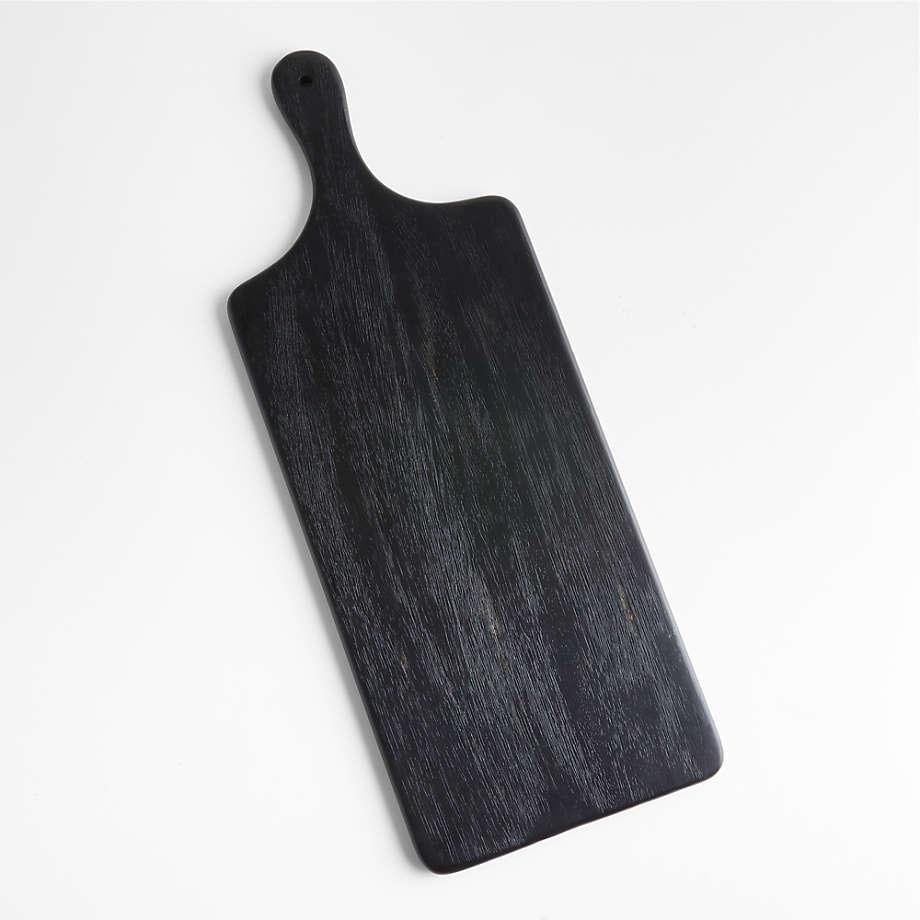 Black-stained oak paddle cutting board with a short rounded handle and visible wood grain, shown flat on a white background; modern rectangular serving board with rounded corners.