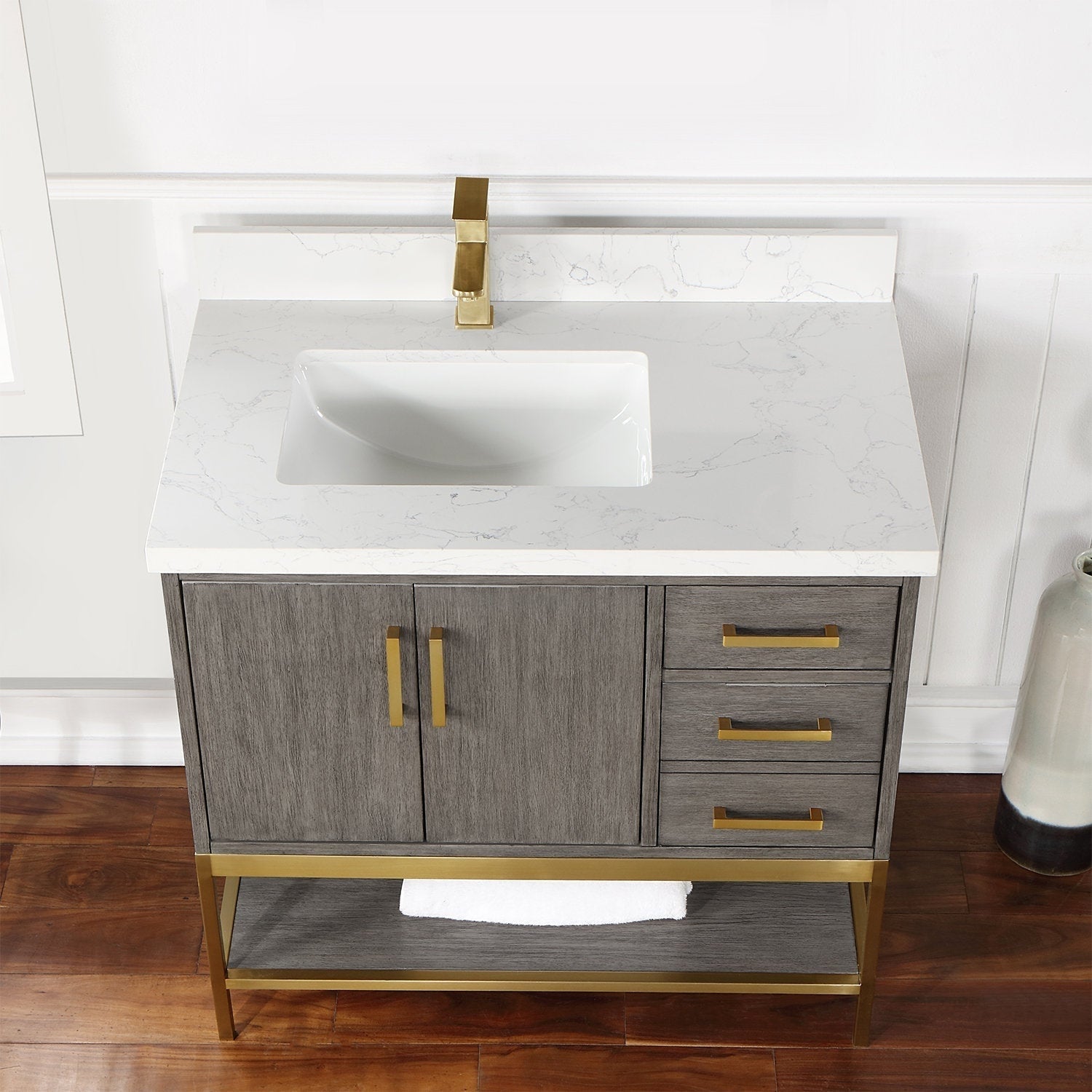 Modern solid wood 36-inch bathroom vanity with a stone top and integrated rectangular ceramic sink, grey wood cabinet, square brass faucet and brass hardware, three right-side drawers, double-door storage and lower open shelf with towel.