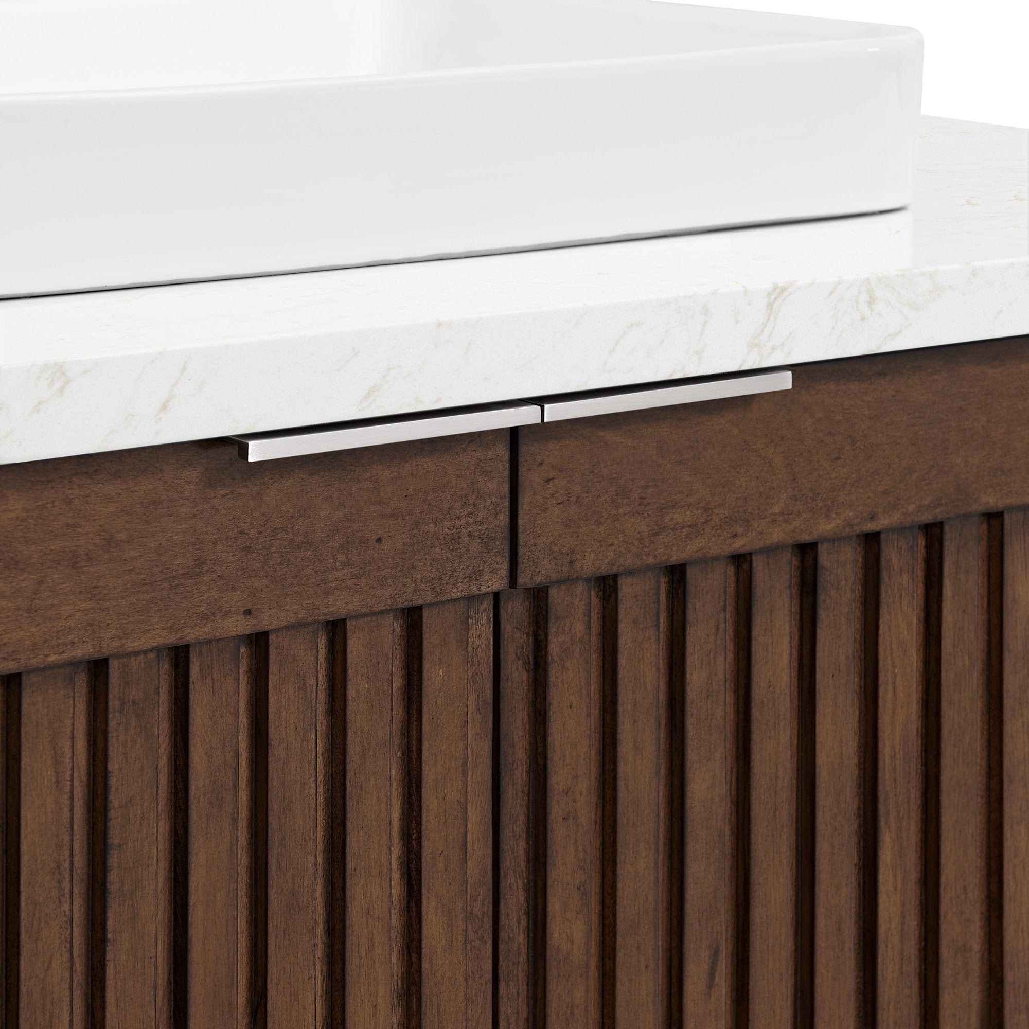 Close-up of a modern bathroom vanity showing a white ceramic vessel sink set on a light stone countertop above a brown natural wood fluted cabinet with slim brushed metal drawer handles.