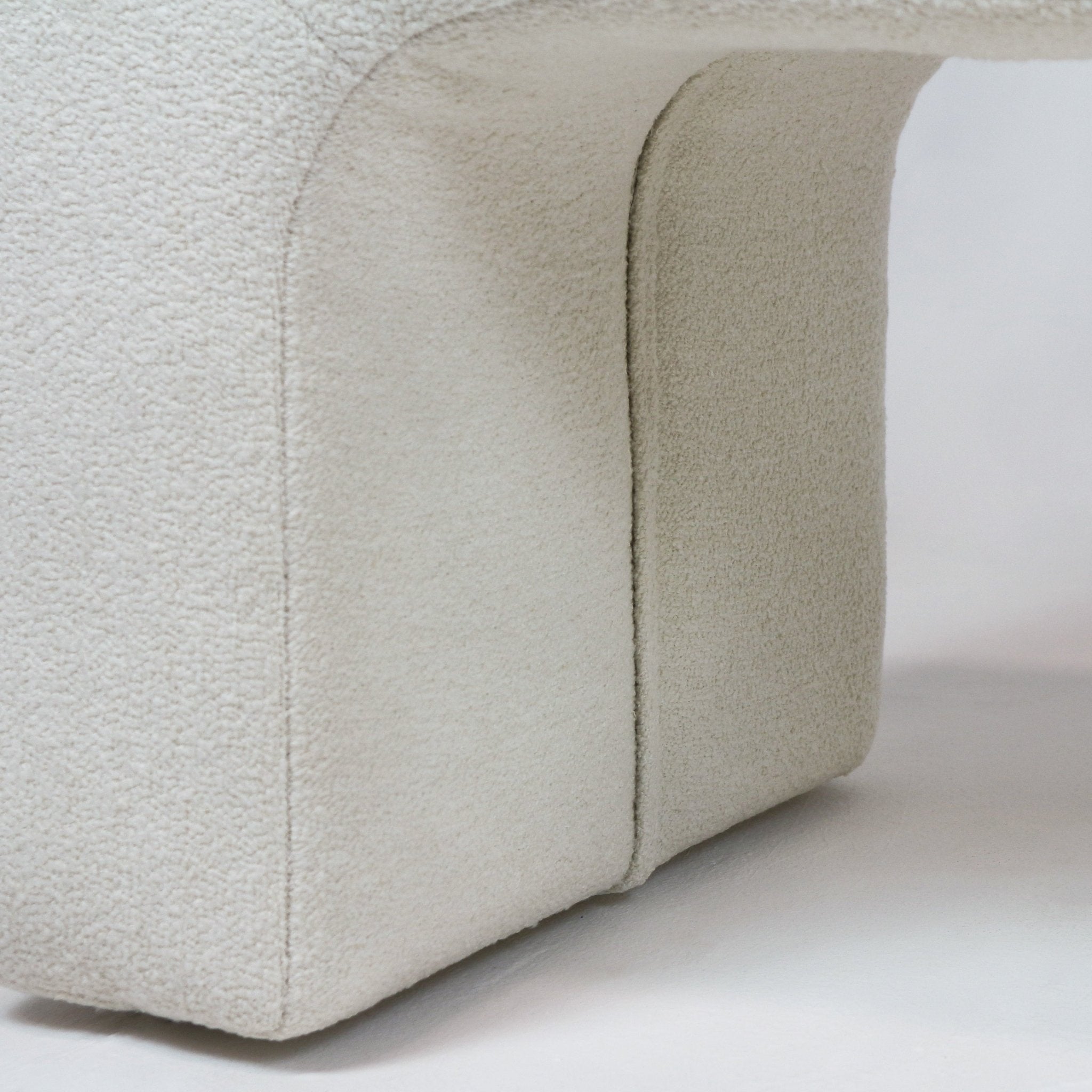 Close-up of an arched bench base upholstered in cream boucle fabric, highlighting the soft textured looped weave, curved seam and minimalist modern coastal profile.