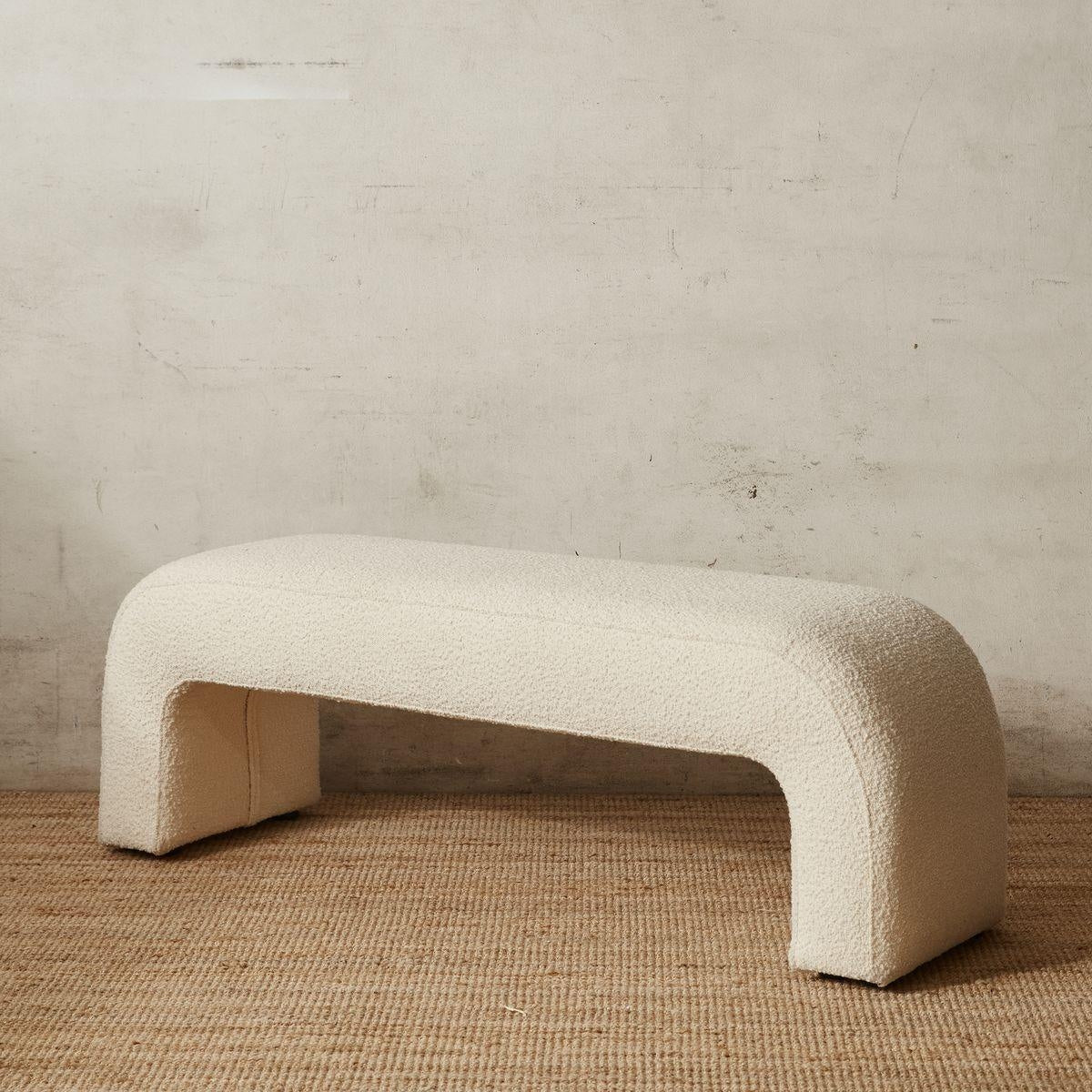 59-inch cream boucle upholstered end-of-bed bench with rounded arch silhouette and integrated U-shaped legs, displayed on a natural jute rug against a textured neutral wall.