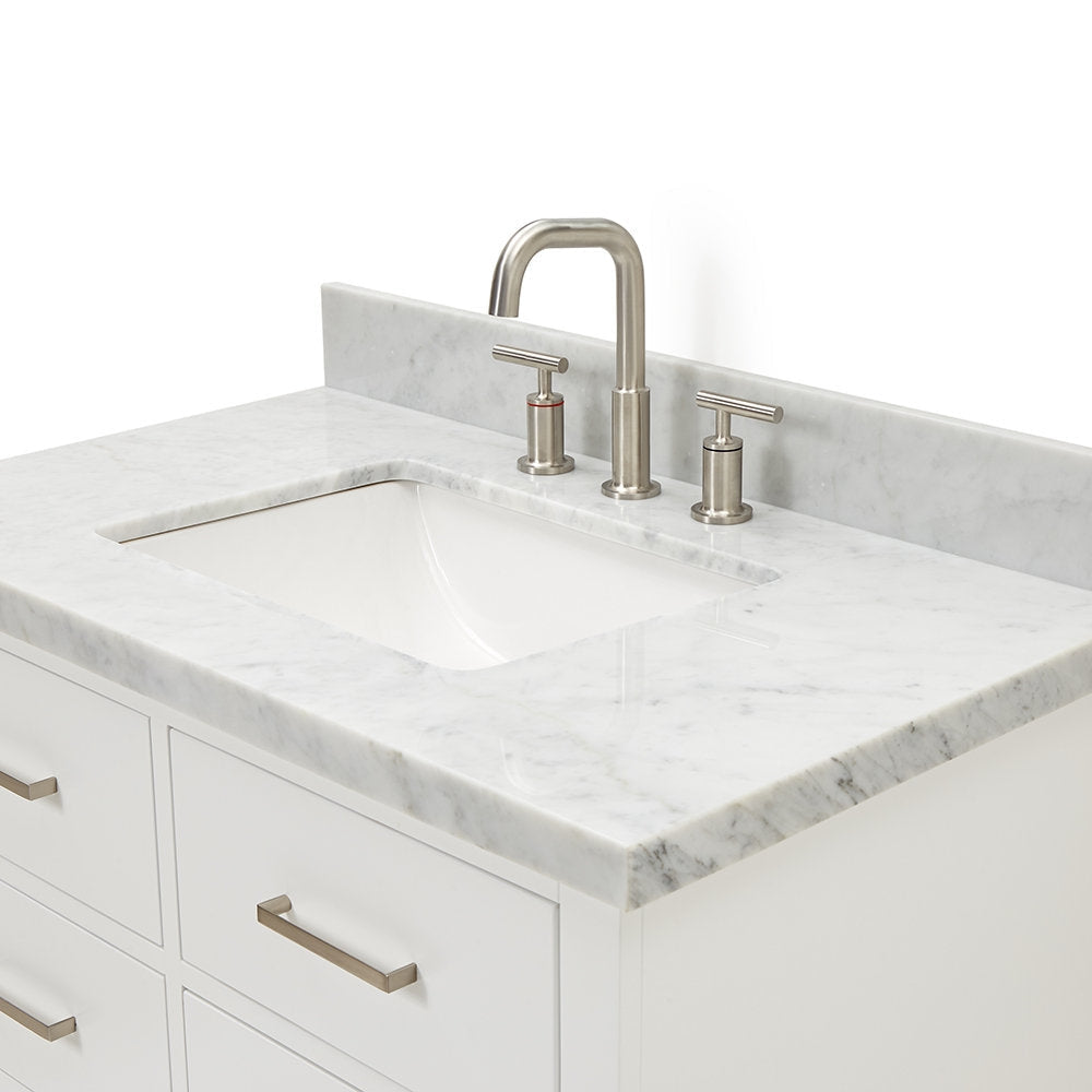 Close-up of a modern white solid wood bathroom vanity with a marble stone countertop, integrated rectangular undermount ceramic sink, low stone backsplash and brushed-nickel three-piece faucet and matching drawer pulls.