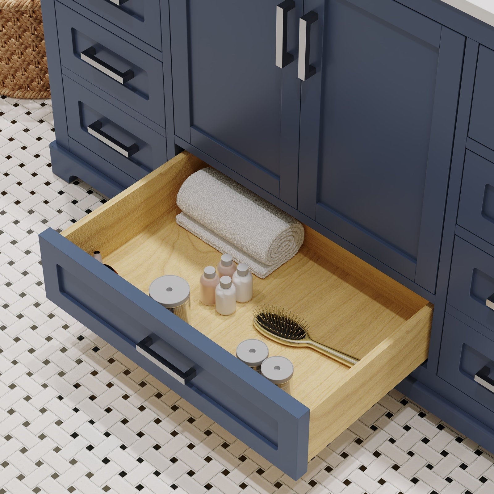 Open drawer of a stone-colored modern bathroom vanity showing a light solid wood interior with a rolled towel, small toiletry bottles, a gold hairbrush and storage jars over a black-and-white mosaic floor.