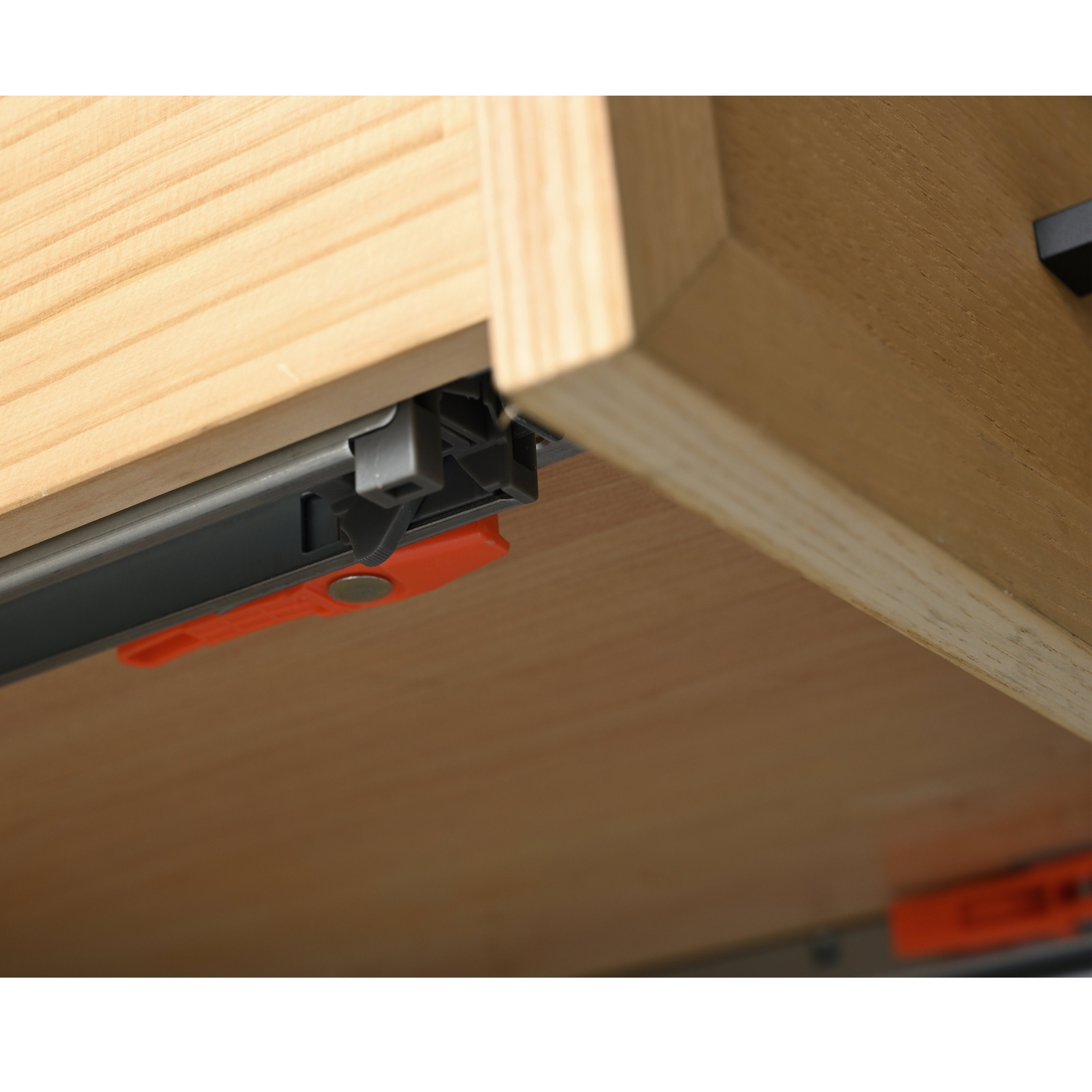 Close-up underside of a bathroom vanity drawer showing solid wood construction, metal soft-close slide hardware and an orange plastic release clip.