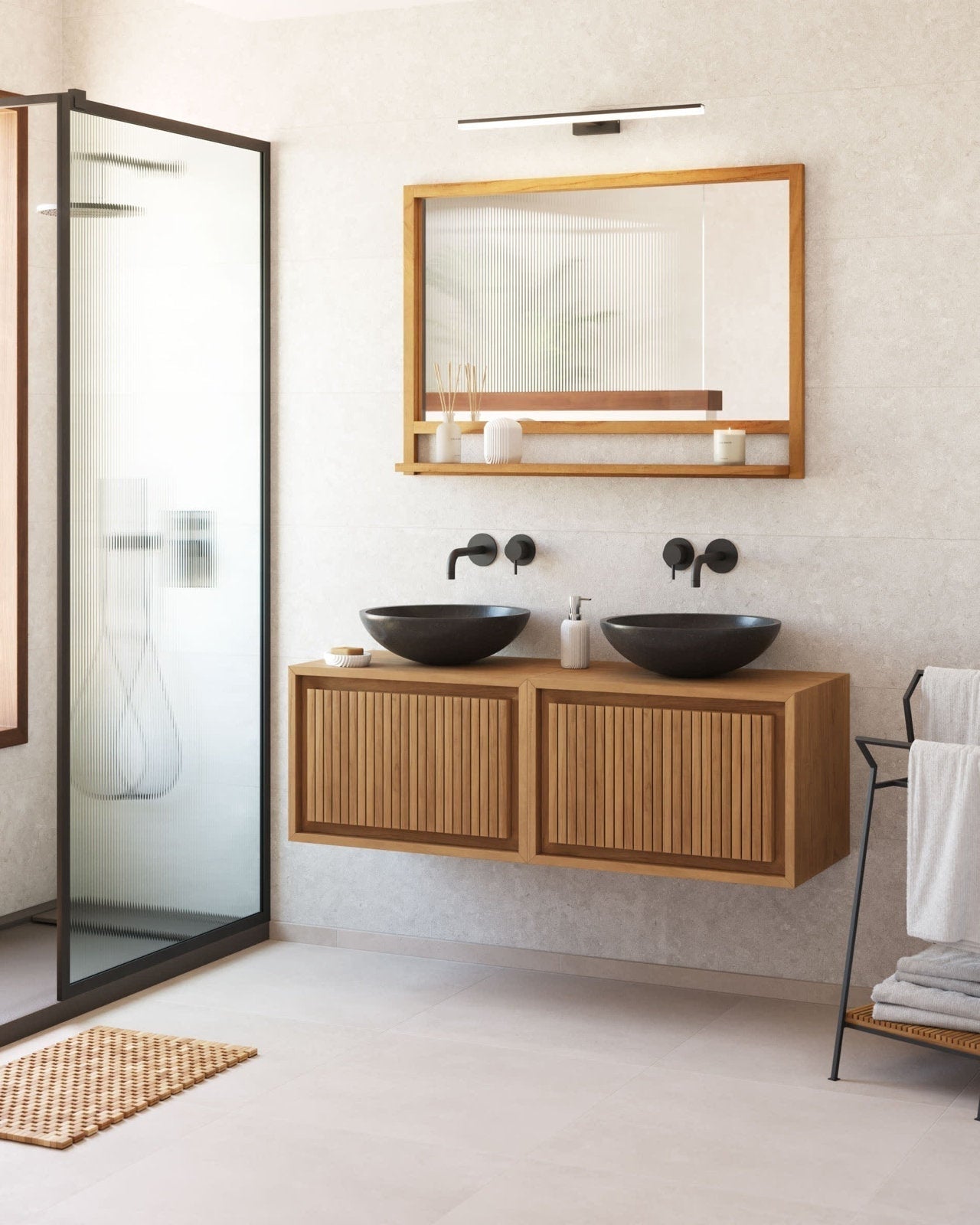 Floating modern solid wood vanity in a natural stone-tone finish with two dark stone vessel sinks, matte black wall-mounted faucets, a wood-framed mirror with shelf above, towel rack at right and frosted glass shower panel at left.