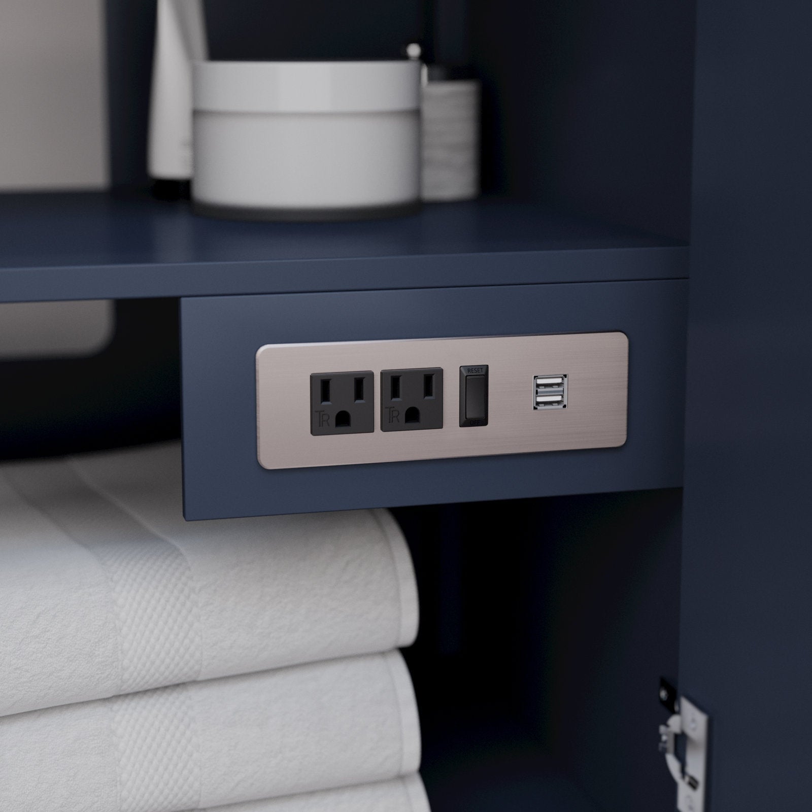 Close-up of a built-in brushed-nickel outlet panel with two grounded power sockets, a reset switch and dual USB ports mounted inside a modern stone-finish solid wood vanity cabinet above folded white towels.