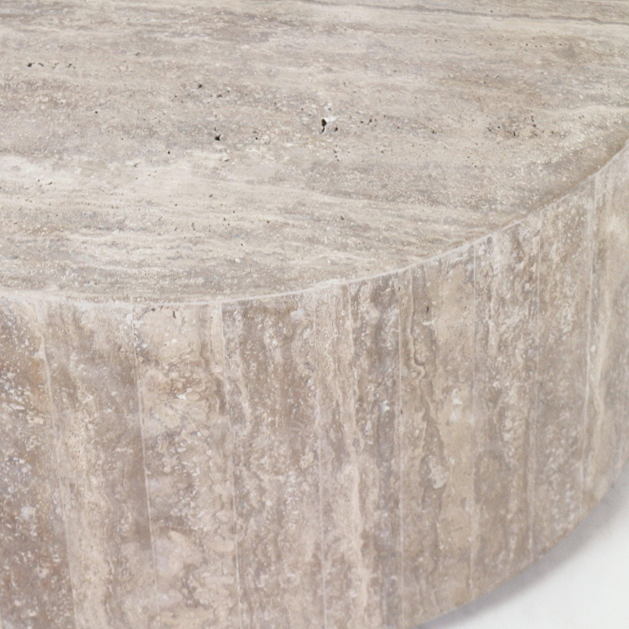 Close-up of a round natural travertine coffee table top and textured vertical banded edge, showing beige veining and a raw stone finish.