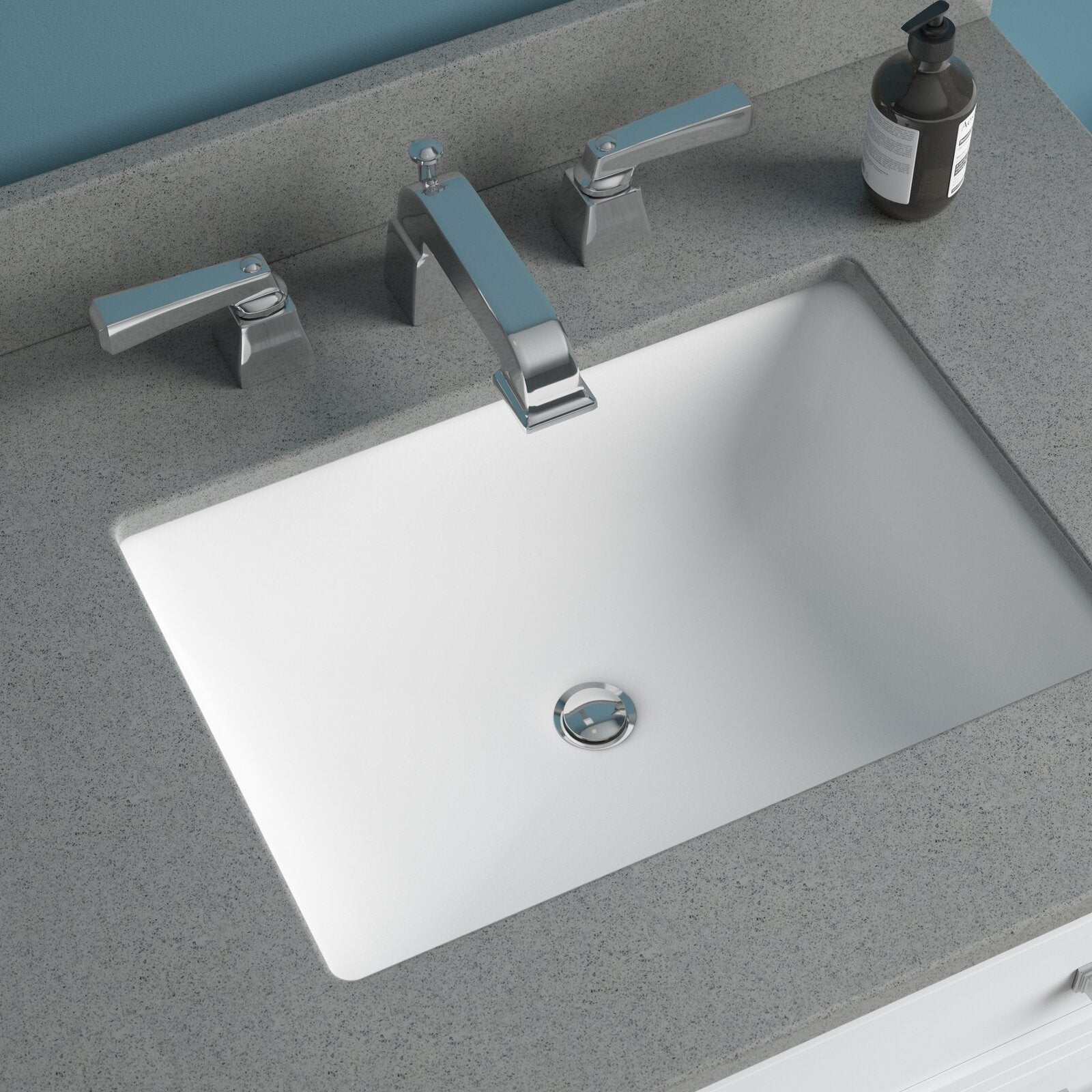White rectangular ceramic undermount sink set in a stone-colored countertop with a chrome three-piece widespread faucet and a dark pump soap dispenser at the rear, shown on a modern bathroom vanity.
