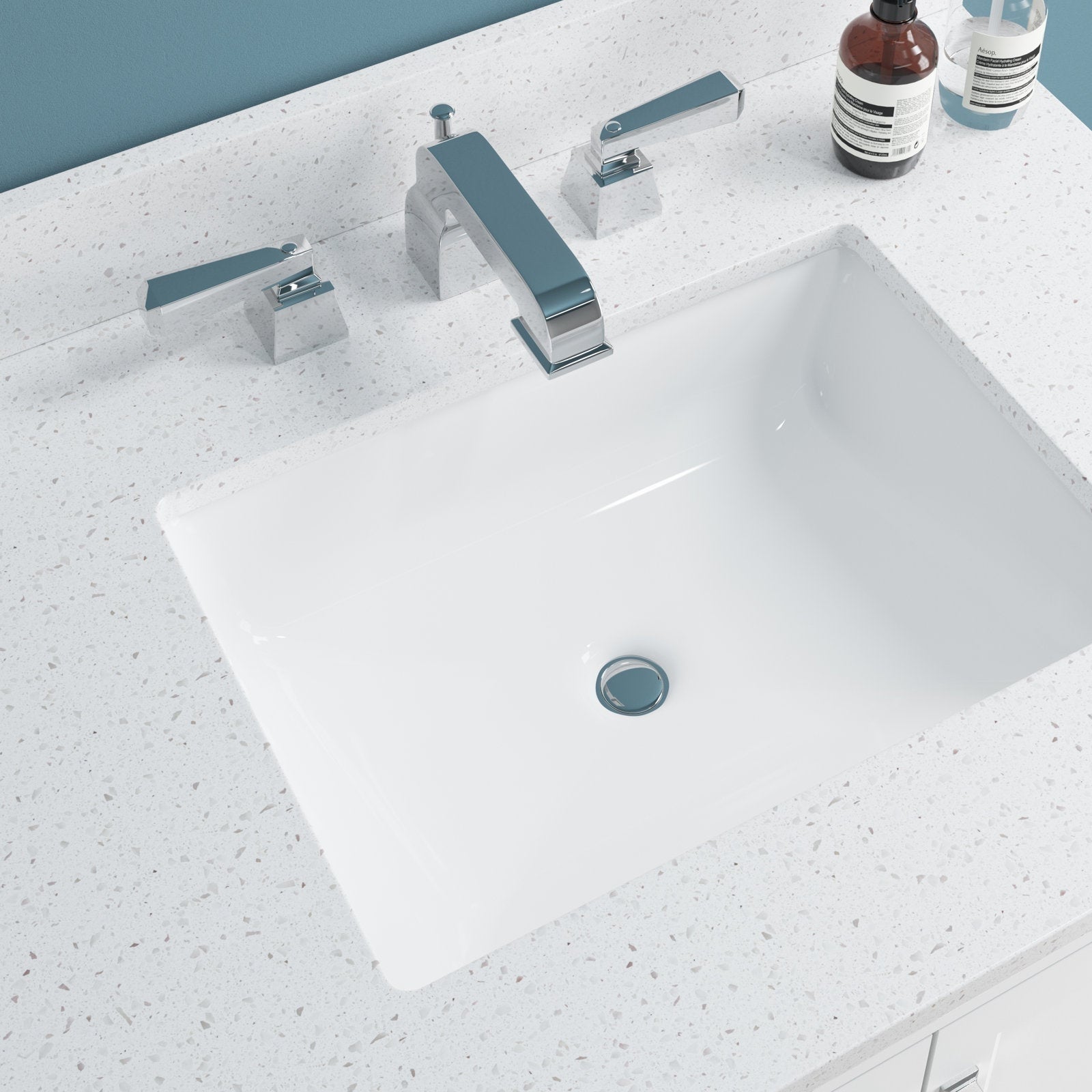 Overhead view of a white rectangular ceramic sink set in a speckled stone countertop with a chrome widespread faucet and two soap bottles on a modern 31-inch single-sink bathroom vanity.