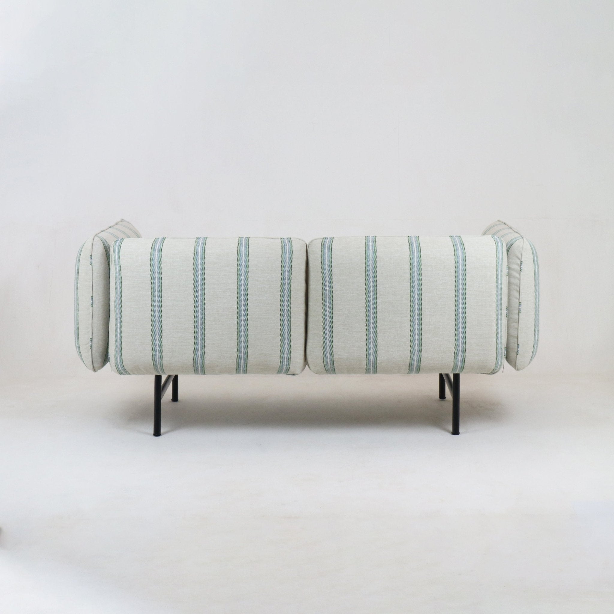 Back view of a modern coastal outdoor sectional upholstered in light neutral fabric with pale green-blue vertical stripes, supported on slim black metal legs.