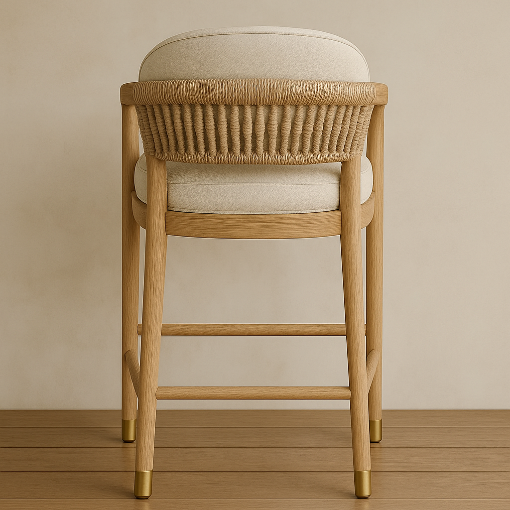 Rear view of a coastal-style bar stool featuring a woven natural rope back, cream upholstered seat and curved teak frame, standing on tapered legs with brass-capped feet on a wood floor.
