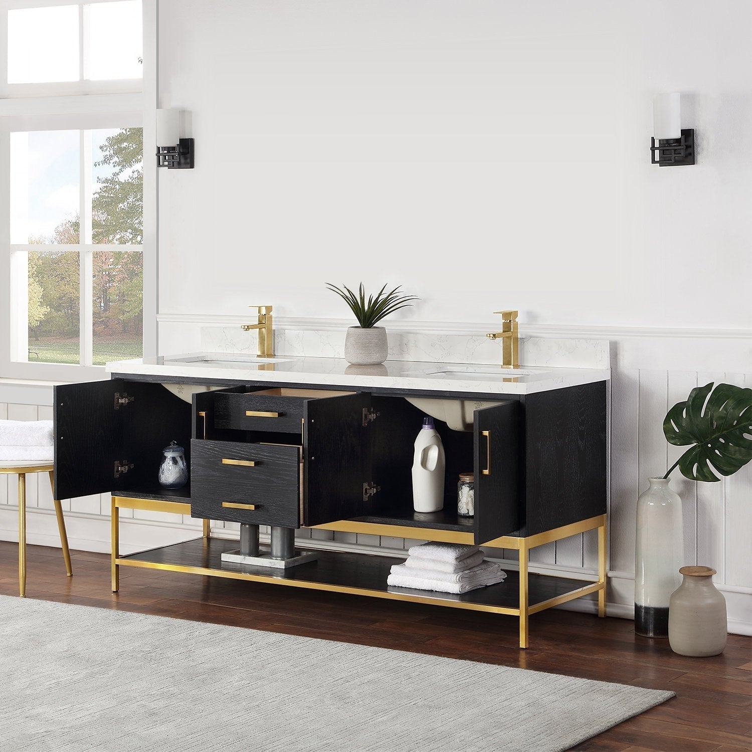 72-inch modern solid wood double-sink vanity with stone countertop, black wood cabinet and gold metal base and hardware, two gold faucets, open drawers and under-sink storage staged with towels, vases and a small plant.