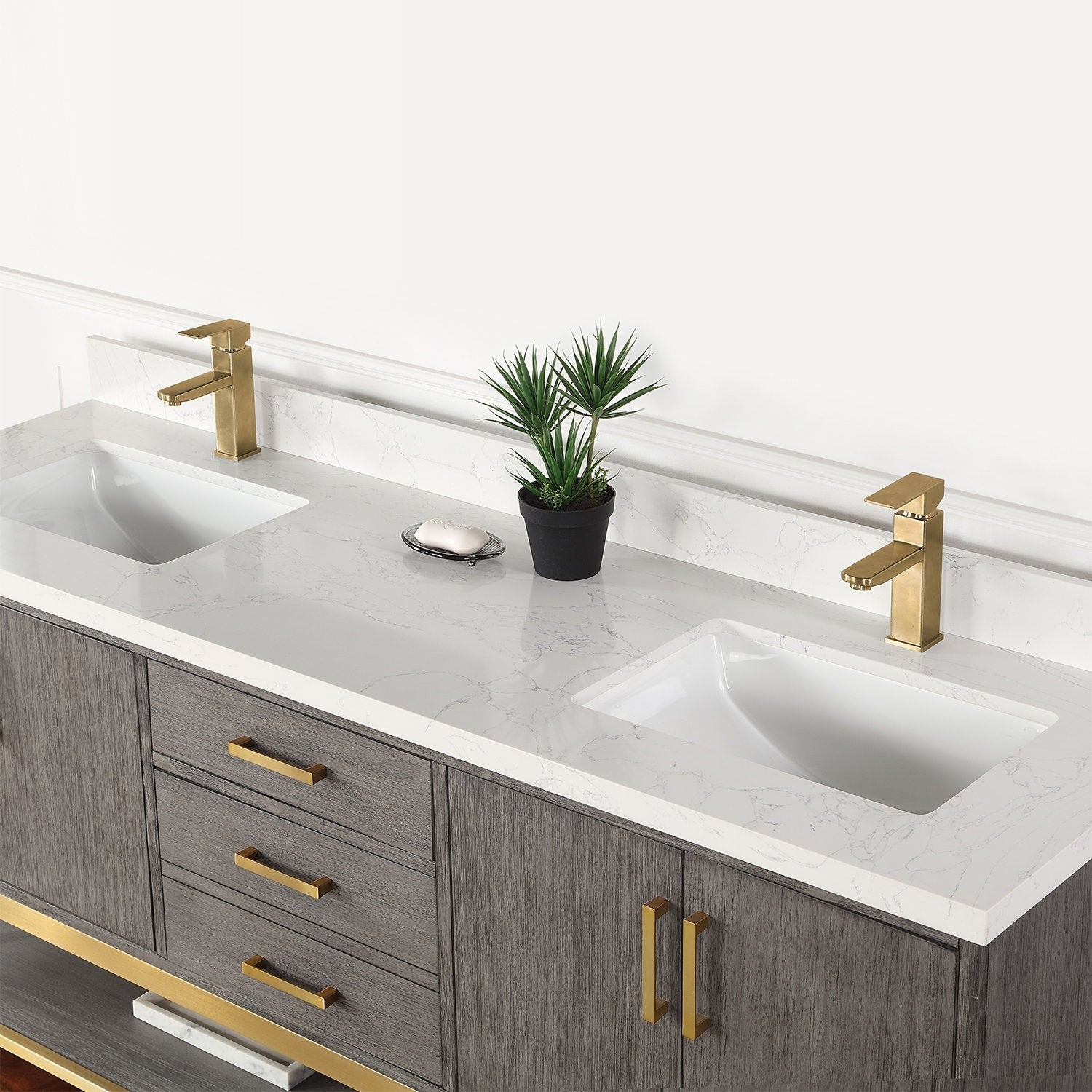 72-inch modern solid wood double-sink vanity with a stone-look white countertop, two rectangular undermount sinks, gold-finish single-handle faucets and matching hardware, gray wood base, small potted plant and soap dish on top.