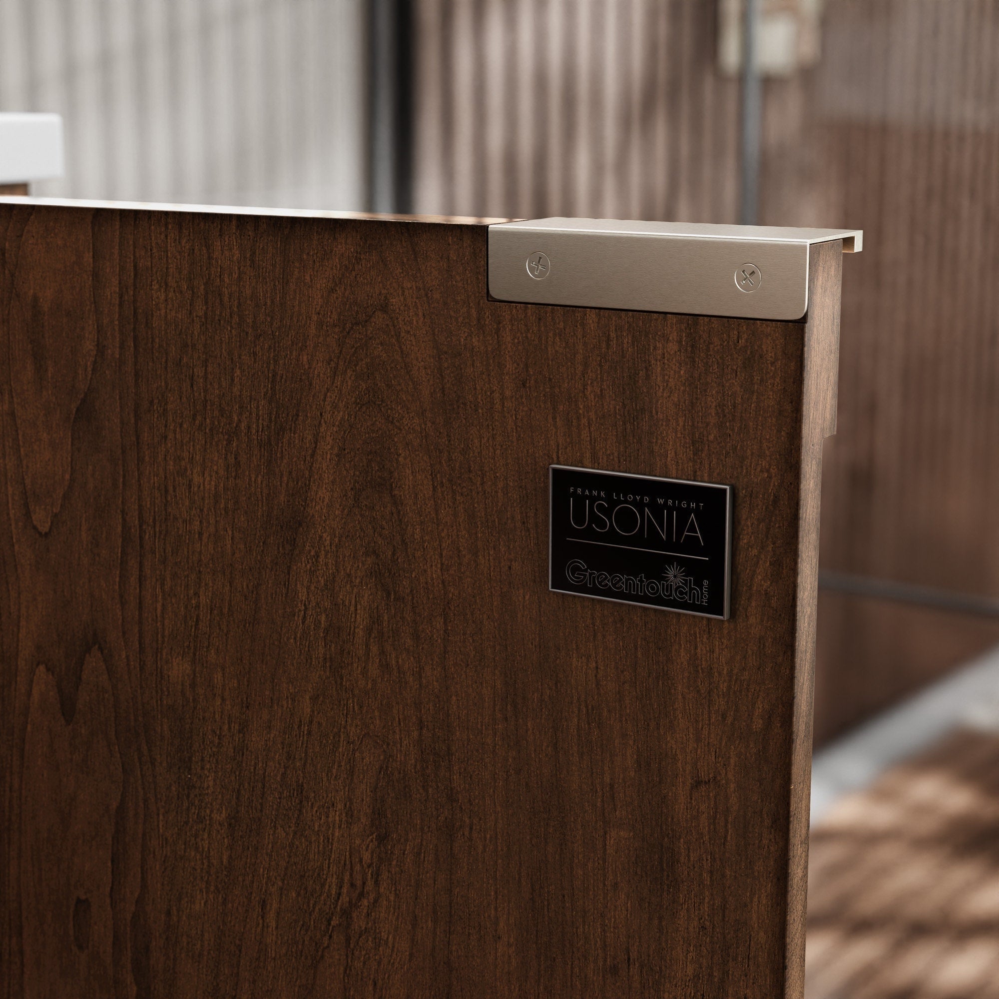 Close-up of a solid wood vanity panel in warm brown with visible grain, showing a stone top edge, brushed metal corner bracket and a small rectangular metal logo plaque mounted on the panel.
