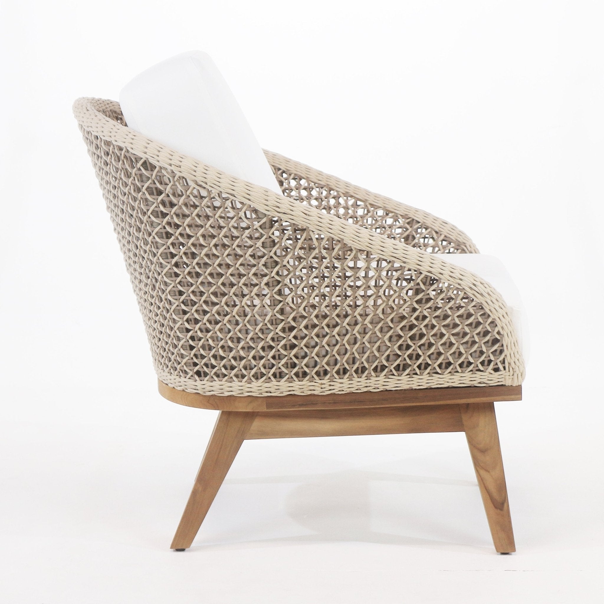 Side profile of a coastal outdoor accent chair with beige rope weave, teak base and angled legs, and white fabric seat and back cushions.