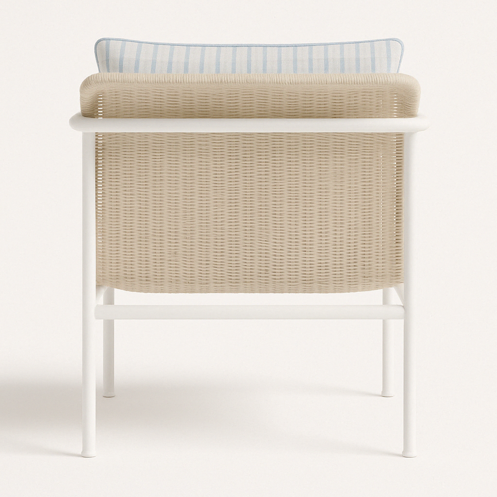 Rear view of an outdoor accent chair with a beige wicker resin back and white aluminum frame, topped by a light blue and white striped cushion with blue piped trim.