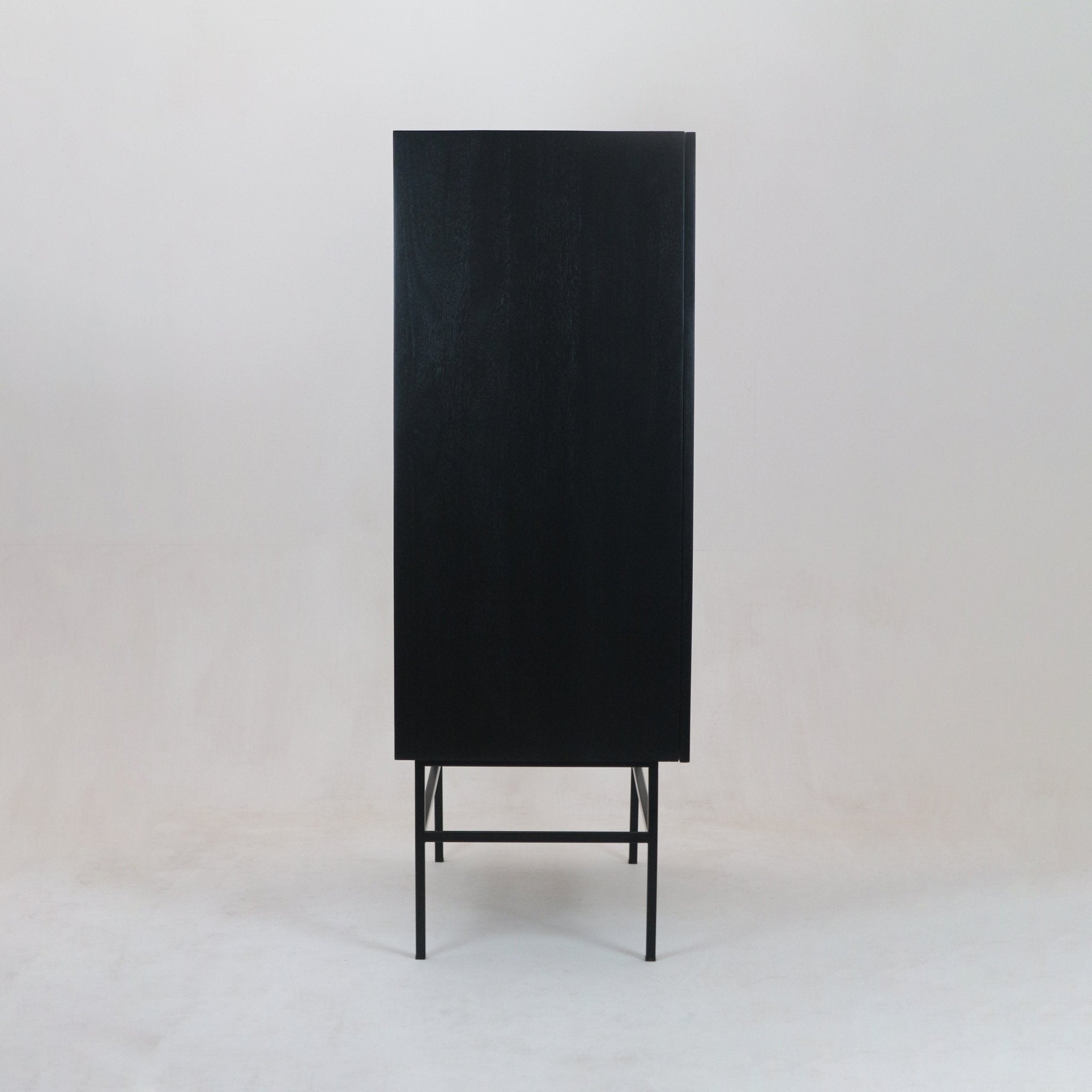 Tall modern wardrobe in black solid wood with a flat door, raised on a slim black metal base and legs, photographed against a neutral studio background.