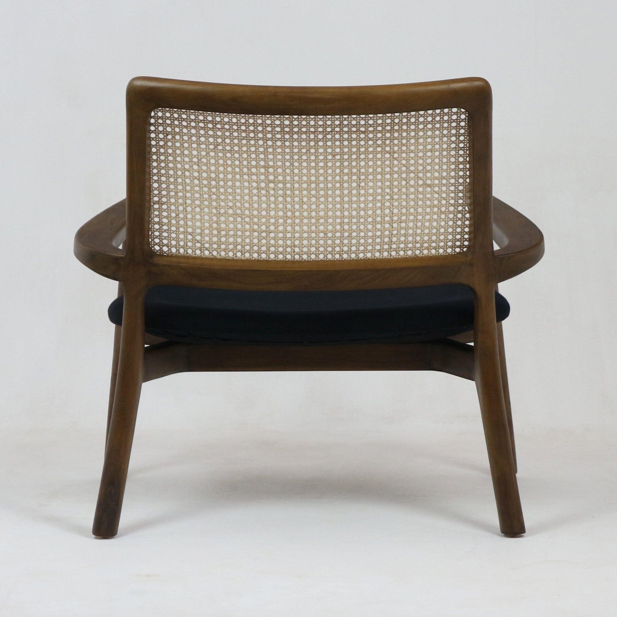 Rear view of a mid-century modern teak lounge chair with a woven cane back and a black upholstered seat cushion on a plain white background.