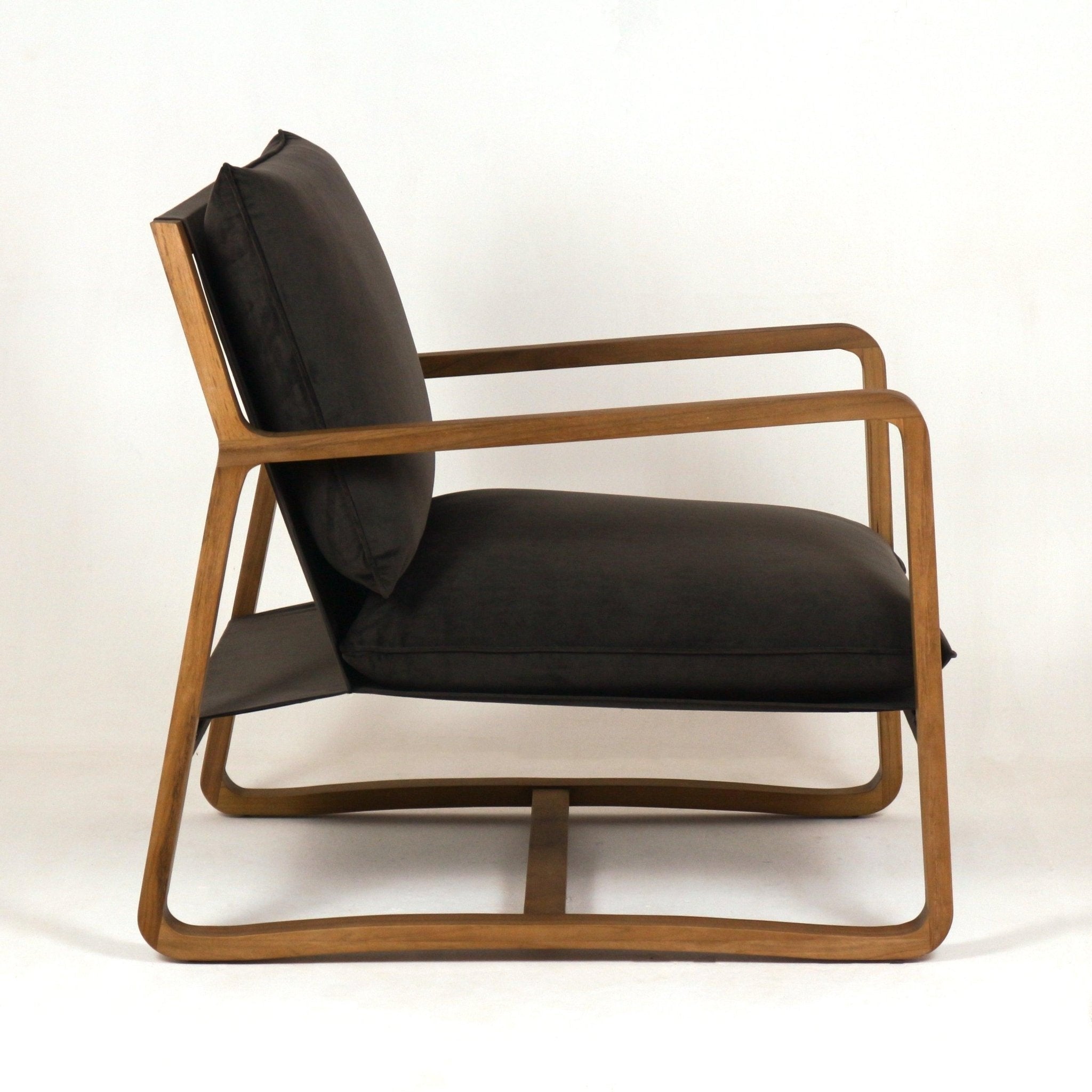 Side view of a mid-century modern accent chair with olive velvet seat and back cushions set in a bent solid oak frame featuring slender sloped arms and a curved sled base.