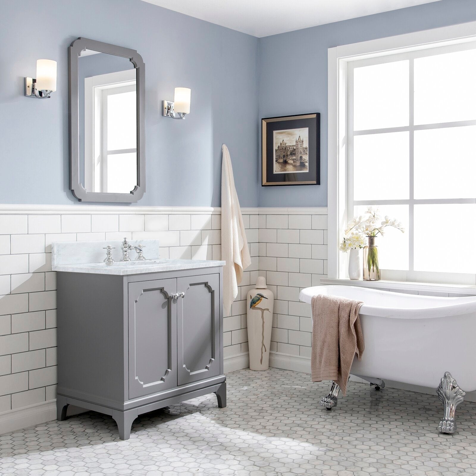 Freestanding solid wood bathroom vanity in soft gray with Carrara white marble countertop, single sink and chrome faucet, shown with mirror, wall sconces and a white clawfoot tub.